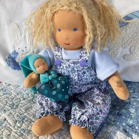 Schlenkerpuppe mit blonden Locken in geblümter Latzhose, ein kleines türkisfarbenes Püppchen im Arm