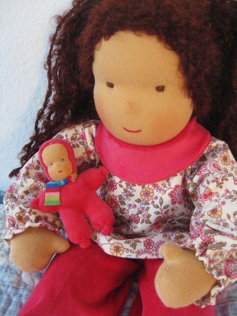 Gliederpuppe mit langen dunkelbraunen Locken in geblümter Bluse und pinkem Halstuch, ein rotes Minipüppchen im Arm