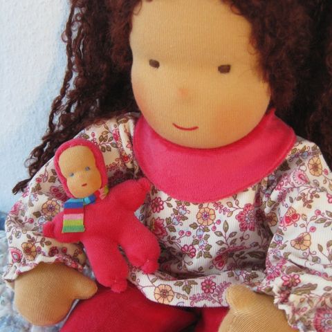 Gliederpuppe mit langen dunkelbraunen Locken in geblümter Bluse und pinkem Halstuch, ein rotes Minipüppchen im Arm