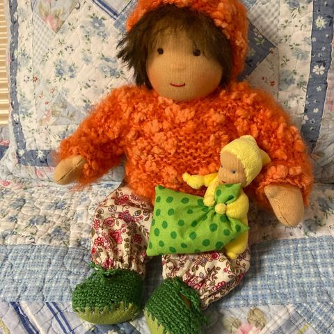 Schlenkerpuppe mit braunem Haar in orangefarbenem Strickpullover mit einem gelben Püppchen