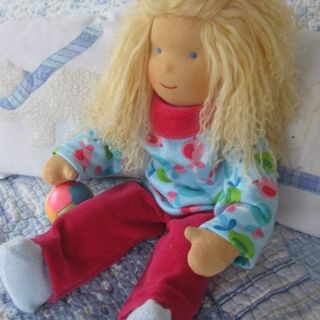 Stoffpuppe mit langem blondem Haar in hellblauem gemustertem Shirt und roter Hose