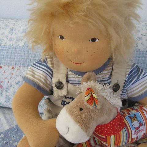 Blonde Babypuppe in Latzhose und Ringelshirt mit einem Stoffpferd