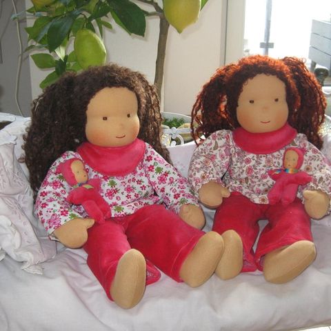 Zwei Gliederpuppen mit braunen Locken in geblümten Blusen und roten Hosen auf einem weißen Sofa