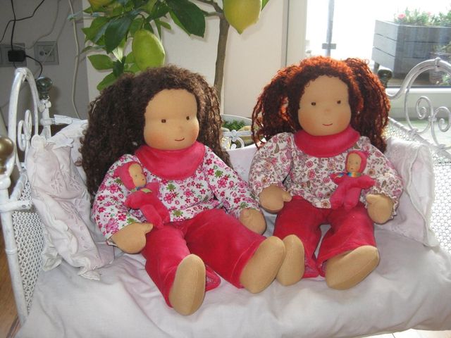 Zwei Gliederpuppen mit braunen Locken in geblümten Blusen und roten Hosen auf einem weißen Sofa
