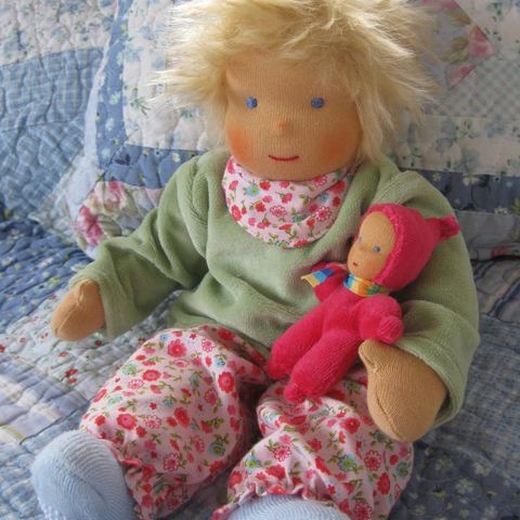 Blonde Gliederpuppe in grünem Pullover und geblümter Hose mit einem roten Minipüppchen