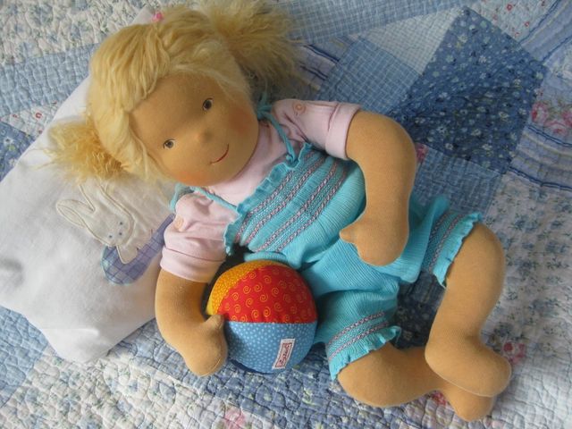 Blonde Babypuppe auf einer Patchworkdecke liegend, mit einem bunten Stoffball