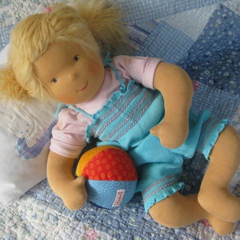 Blonde Babypuppe auf einer Patchworkdecke liegend, mit einem bunten Stoffball