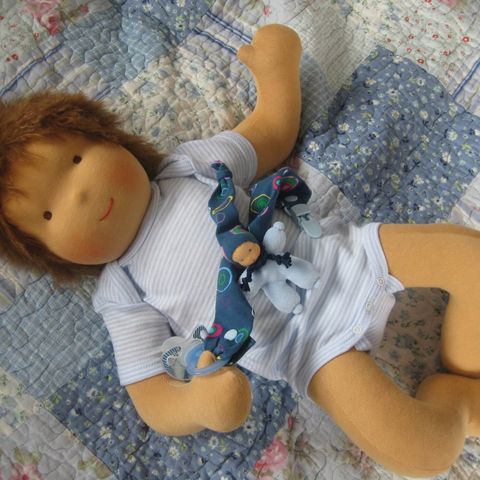 Babypuppe mit braunem Haar im weißen Body auf einer Patchworkdecke liegend