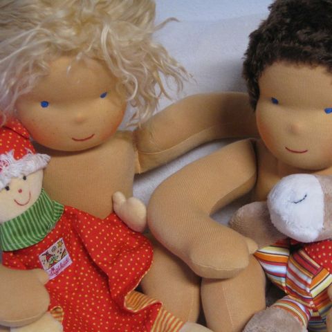 Zwei Babypuppen, blond und dunkelhaarig, mit Kuscheltieren