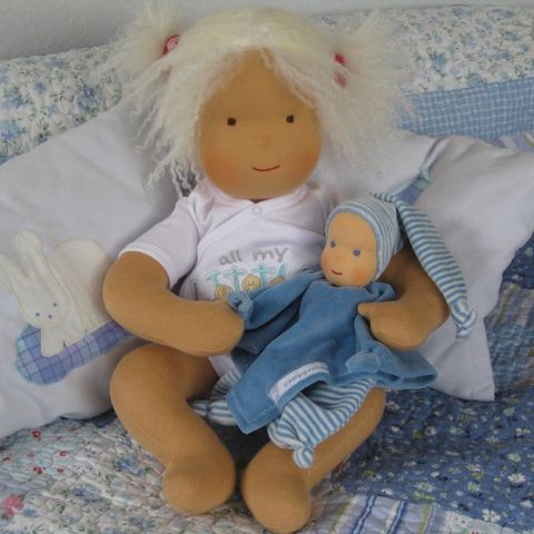 Weißblonde Gliederpuppe an ein Kissen gelehnt, ein kleines Babypüppchen im Arm