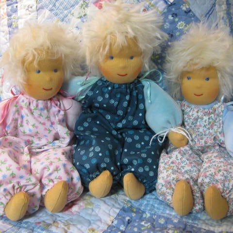 Drei blonde Nickipuppen in geblümten Anzügen auf einer Patchworkdecke