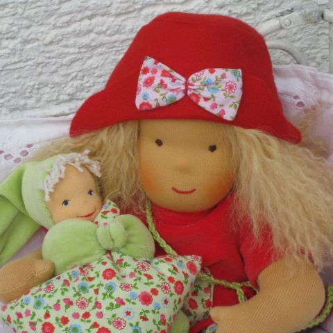 Blonde Gliederpuppe mit rotem Hut und Stoffschleife neben einem Püppchen mit grüner Zipfelmütze