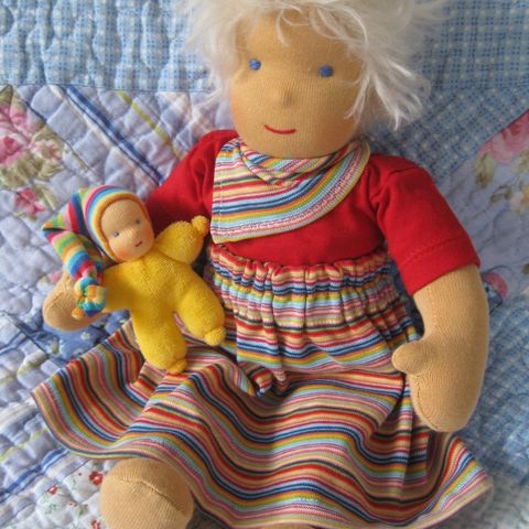 Weißblonde Schlenkerpuppe im Ringelrock mit einem gelben Püppchen