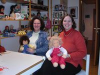 Zwei Frauen in einem Zimmer voller Puppen, jede mit einer fertigen Stoffpuppe auf dem Schoß
